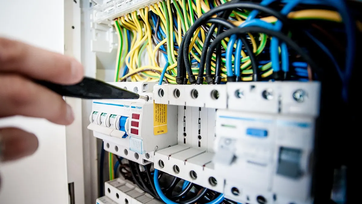 Mão testando disjuntores em quadro elétrico com fios coloridos
